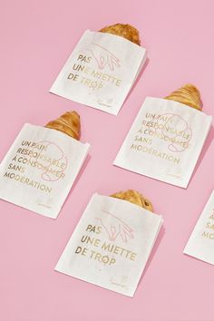 four white paper bags filled with croissants on top of a pink surface