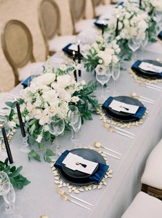 a long table is set with black and white plates, silverware, and flowers