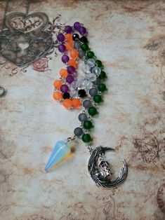 This set of prayer beads was made with Samhain in mind. This set of beads features colorful beads, a gemstone pendulum, and a silver-toned metal charm or charms. These prayer beads can be used as prayer or meditation beads, or for pendulum dowsing. These beads are made with Pagans, Wiccans, Witches, Druids, Heathens, and other Pagan groups in mind, but could be used by anyone who loves and has a deep reverence for the Earth. The beads are hand-wired using silver-toned stainless steel eye pins. T Spiritual Crystal Necklaces With Moon Charm For Festivals, Handmade Spiritual Crescent Crystal Necklace, Handmade Crescent Crystal Necklace With Spiritual Style, Handmade Spiritual Czech Glass Crystal Necklace, Spiritual Silver Crystal Necklace With 8mm Beads, Spiritual Czech Glass Natural Stone Crystal Necklaces, Pagan Prayer Beads, Pagan Prayer, Types Of Prayer