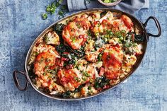 a pan filled with chicken, spinach and cheese on top of a blue table