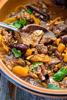 a bowl filled with meat and vegetables on top of a wooden table next to a spoon