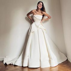 a woman standing in front of a white wall wearing a dress with a bow at the waist