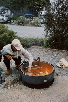 a man with a hat is cooking something in an open fire pit on the ground