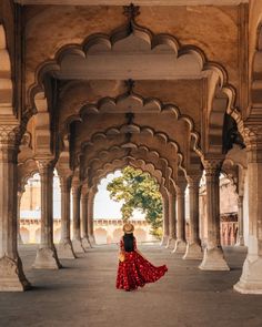 a woman in a red dress is standing under an archway with columns and arches on both sides