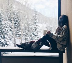 a woman sitting on a window sill holding a cup in her hand and looking out the window