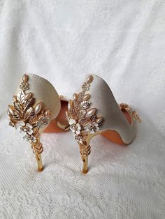 two pairs of wedding shoes with gold and white flowers on them, sitting on a lace covered surface