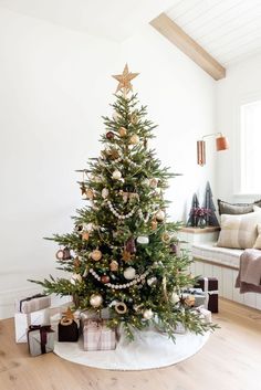 a decorated christmas tree in a living room with white walls and wooden flooring,