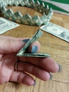 a person holding money in their hand on top of a wooden table next to other dollar bills