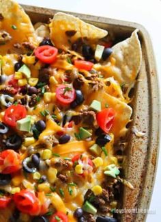 nachos with cheese, black olives, and tomatoes in a casserole dish