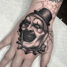 a hand with a tattoo on it that has a clown's face and spider web