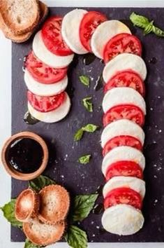 sliced tomatoes, mozzarella and basil on a cutting board with olives next to them