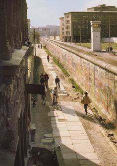 people walking and riding bikes on a city street next to a wall with graffiti written on it