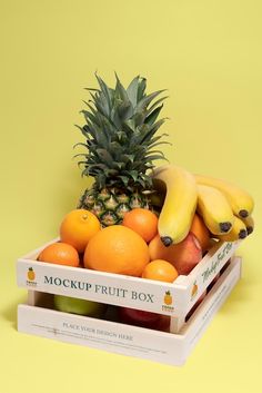 a pineapple, oranges and bananas are in a box on a yellow background