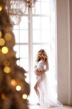 a pregnant woman poses in front of a christmas tree