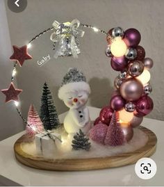 a snowman and christmas tree made out of ornaments on a wooden board with lights