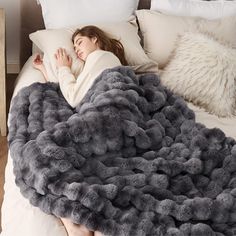 a woman laying in bed under a fluffy gray blanket