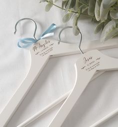 two wedding hangers with names on them and a bouquet of flowers in the background