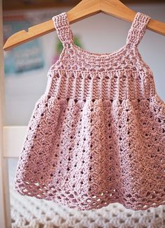 a pink crocheted dress hanging on a wooden hanger next to a bed