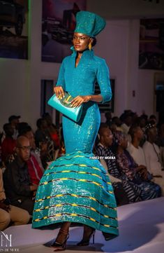 a woman is walking down the runway wearing a blue dress and matching headdress