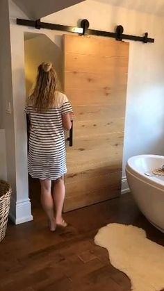 a woman standing in front of a bathtub next to a white tub and wooden floor