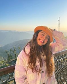 a woman wearing a hat standing on top of a metal balcony next to a mountain