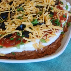 a pizza topped with cheese and olives on a white plate next to a blue table cloth