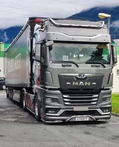 a large semi truck parked in a parking lot next to a building with mountains in the background