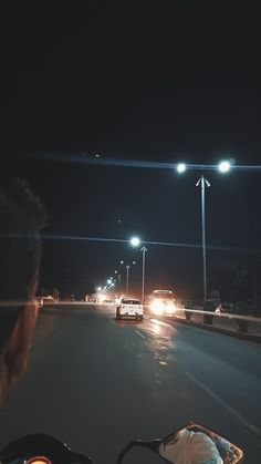 a man driving down the road at night with his bike in front of him and cars behind him