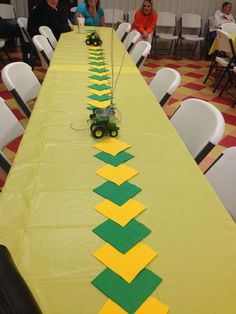 a long table with yellow and green paper on it, along with people sitting at tables in the background