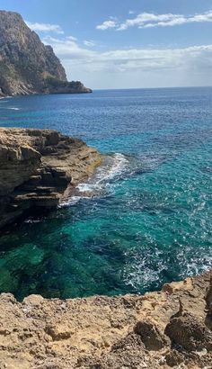 the ocean is clear and blue with waves coming in from the rocks on the shore