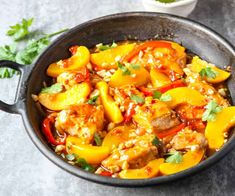 a skillet filled with chicken and peppers on top of a table next to a bowl of cilantro