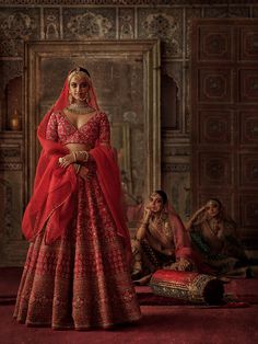 a woman in a red and gold bridal gown standing next to two other people