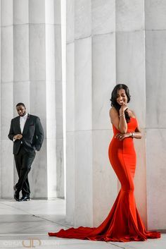 a woman in a red dress standing next to a man in a tuxedo