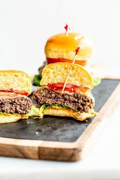 two hamburgers on a cutting board with toothpicks in them