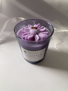 a purple candle with a flower in it sitting on a table next to some white fabric