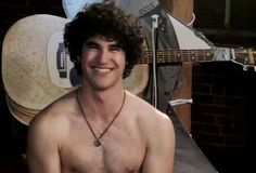 a shirtless young man standing in front of a guitar