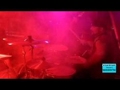 a man playing drums in front of purple and red lights