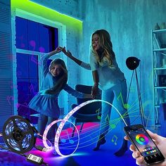 two girls are playing with an interactive light up projector while someone holds their cell phone in front of them