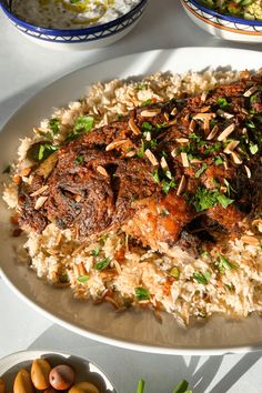 a white plate topped with rice covered in meat and veggies next to bowls of fruit