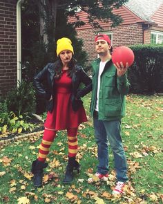 a man and woman dressed up in costumes standing on the grass with a red ball