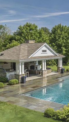 an outdoor kitchen next to a pool in the middle of a lush green yard with trees