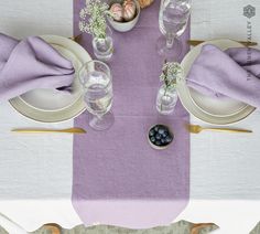 the table is set with plates, silverware and purple napkins for an elegant dinner