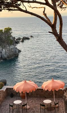 an outdoor dining area overlooking the ocean with umbrellas and tables set up for two