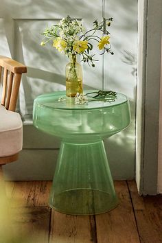 a vase with flowers sitting on top of a glass table next to a chair and door