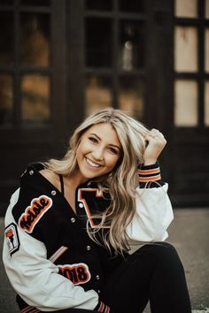 a woman sitting on the ground wearing a black and white jacket with an orange logo