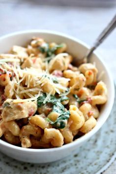 a white bowl filled with pasta and spinach on top of a blue place mat