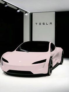 a pink car is parked in front of a wall with a tesla logo on it