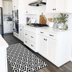 a kitchen with white cabinets and black and white area rugs on the hardwood floor