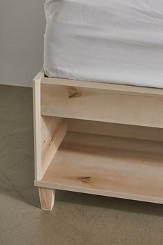 a bed with a white sheet on top of it and a wooden shelf next to it