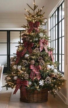 a christmas tree with bows and pine cones in a basket on the floor next to a window